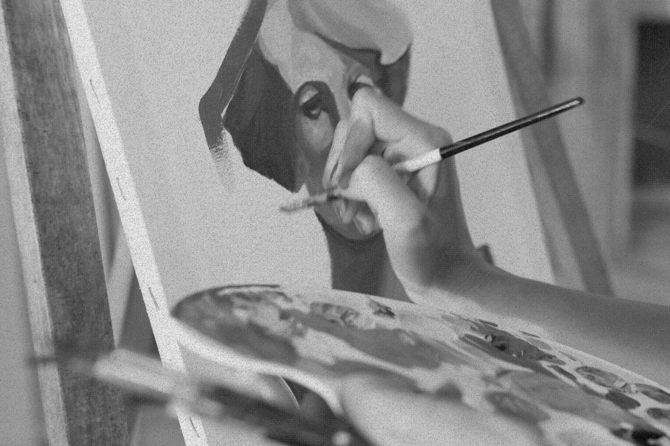 Imagen de un primer plano de las manos de Natalia mientras pinta sobre un lienzo y sujeta con la mano izquierda una paleta de pintura